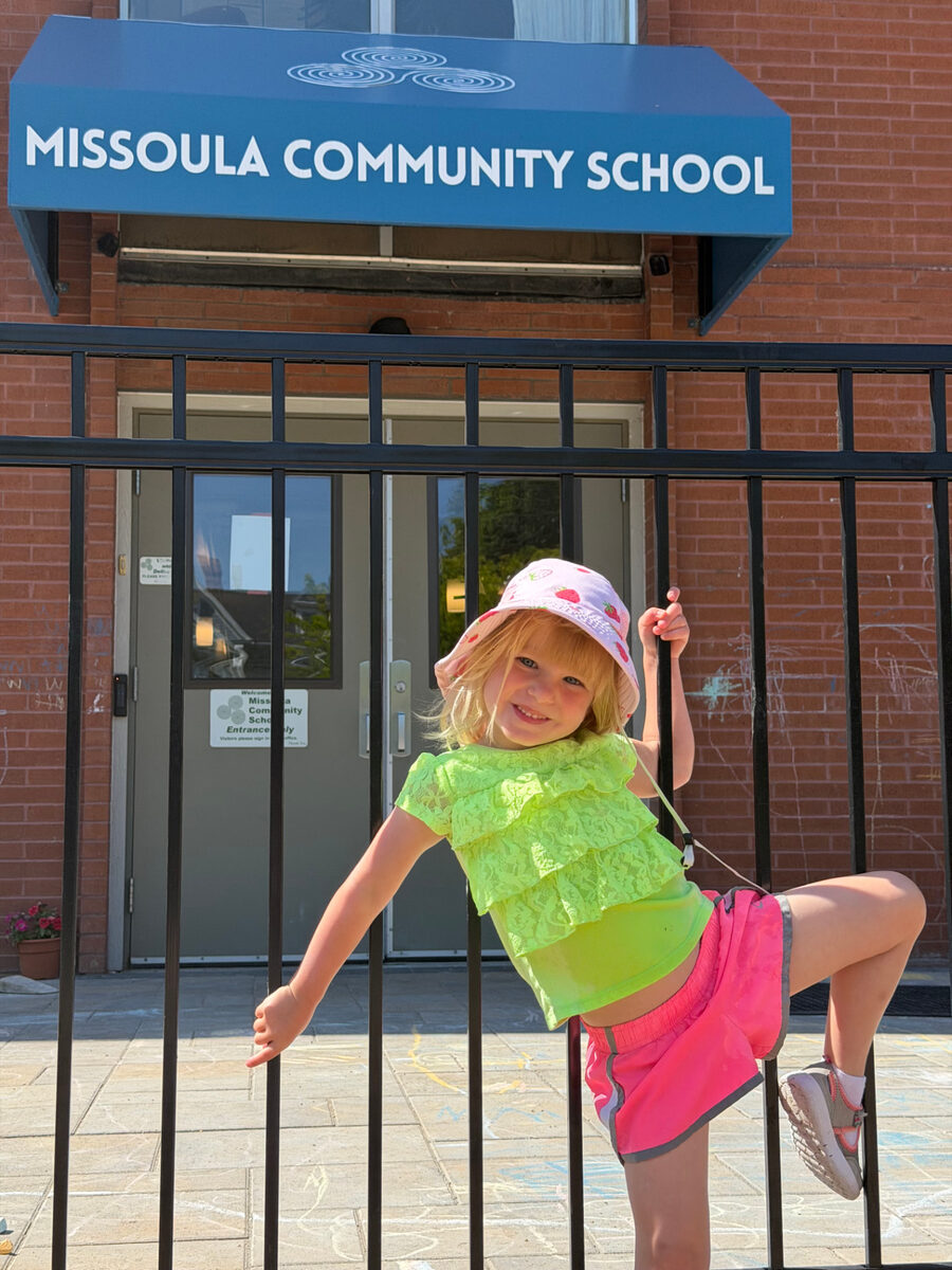 A learner in a green shirt climbs the fence in front of the Missoula Community School entrance